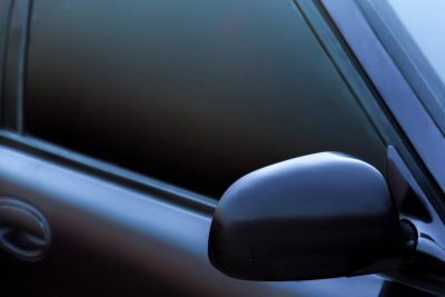 Side mirror and tinted window of a black car.