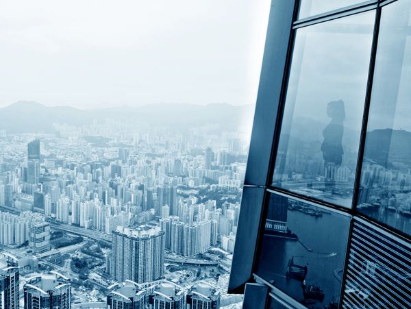 Cityscape reflection on a skyscraper window with a person's silhouette.
