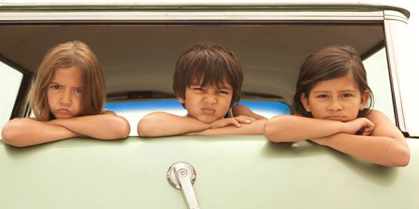 Three kids making funny faces leaning out of a car window.