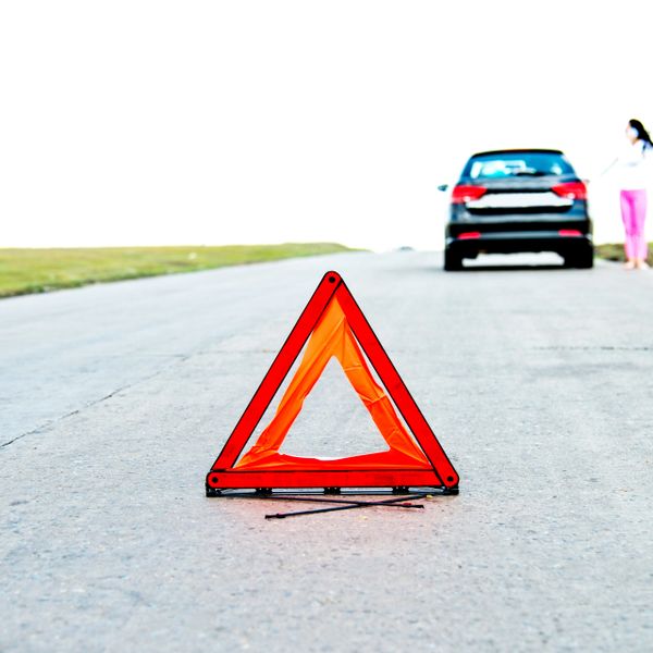 Warning triangle placed on road with a car and person in the background.