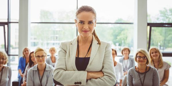 Confident woman leader standing with a team behind her in a bright office.