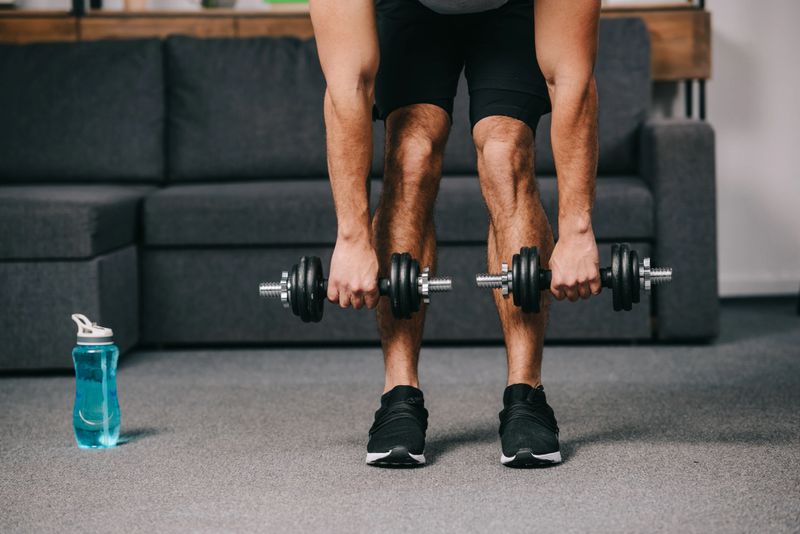 cropped view of strong muscular man workout with dumbbells in home gym