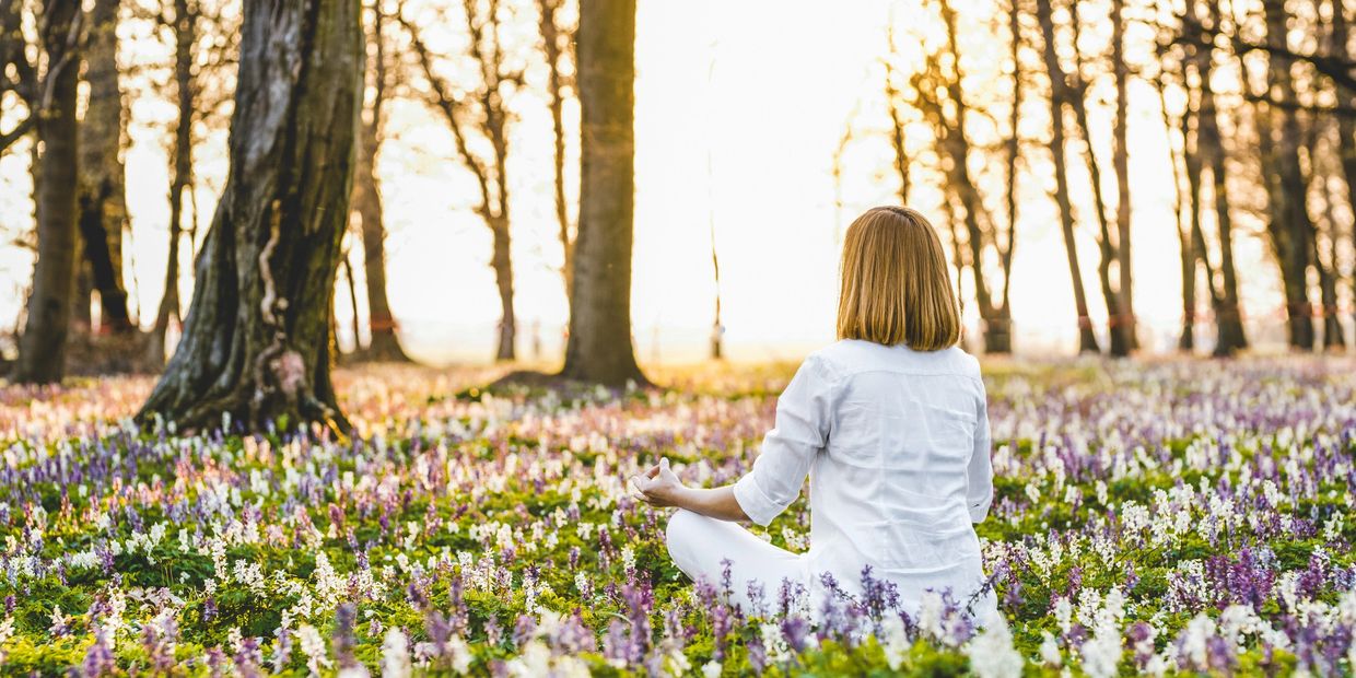 Woman in white sitting in a meditative pose in a forest with wild lavender all around her