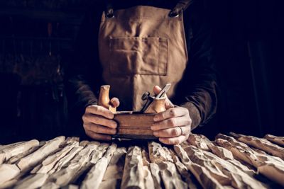 Craftsman holding a wooden hand plane over carved wood pieces.