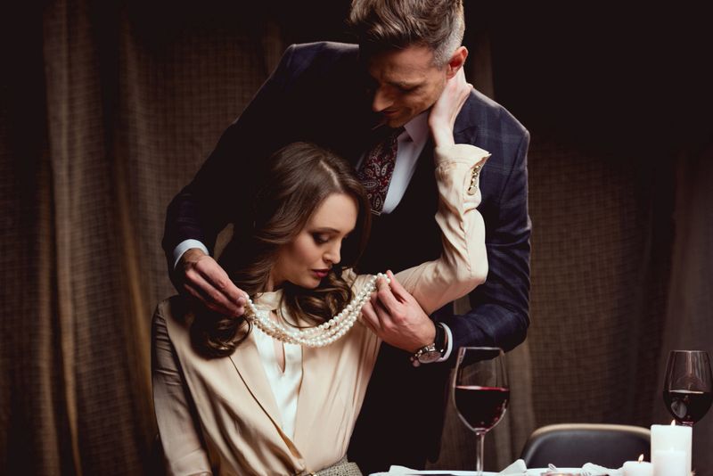 man putting pearl necklace on beautiful woman during romantic date in restaurant