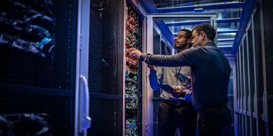 Dois profissionais analisando servidores em data center.