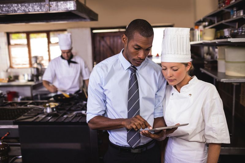 Male manager and female chef using digital tablet in kitchen at hotel