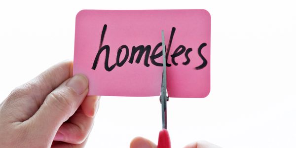 Scissors cutting a card with the word 'homeless' to symbolize ending homelessness.