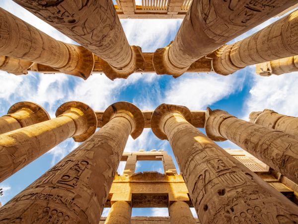 Ancient Egyptian columns with hieroglyphs under a blue sky.