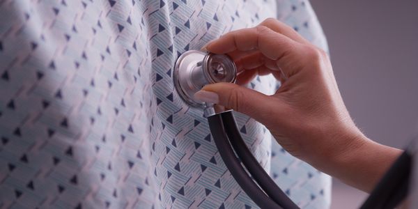 Hand holding a stethoscope on a patient wearing a patterned hospital gown.