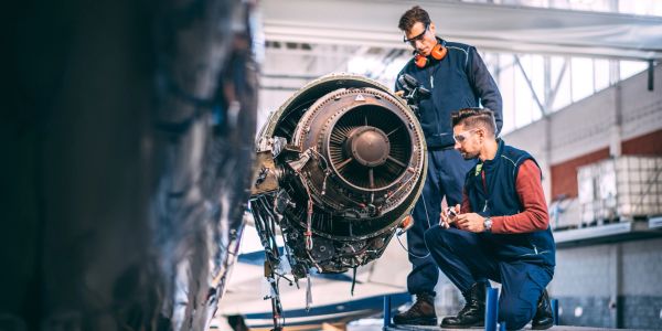 Dos técnicos inspeccionan un motor de avión en un hangar.