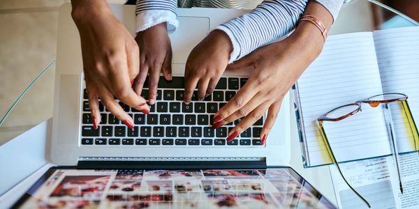 Child and adult typing together on a laptop keyboard at a glass table.