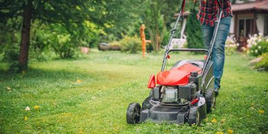 Person mowing a green lawn with a red lawnmower.