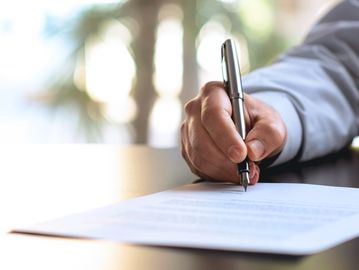 A person signs a document with a pen on a desk.