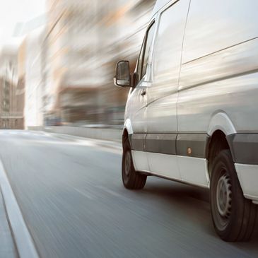 White delivery van speeding on a city street with motion blur.