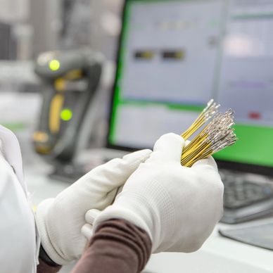 Person wearing white gloves holding fiber optic cables in a lab setting.