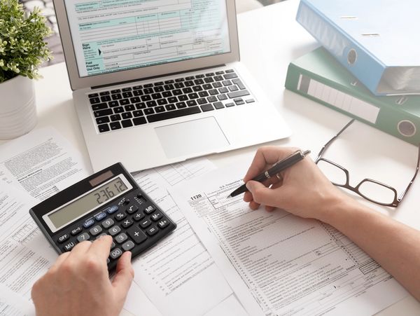Person calculating taxes with calculator and forms on a desk.
