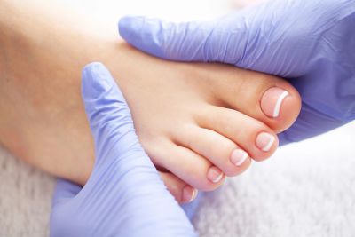 Gloved hands examining a person's foot for medical care.