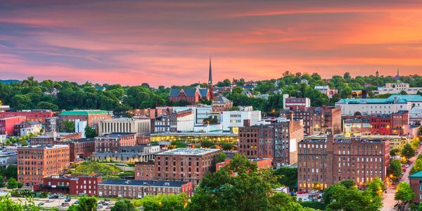Panoramic view of a city skyline at sunset with vibrant orange and purple skies.
