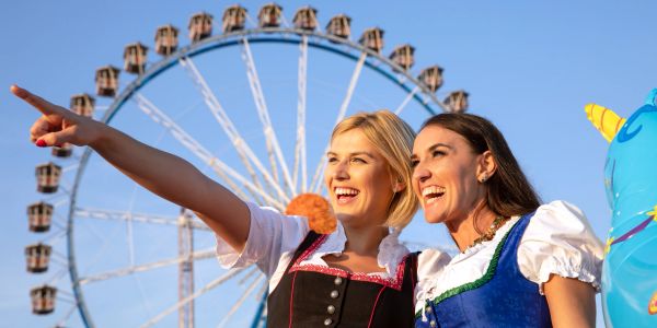 Two women in traditional dresses at a fair with a Ferris wheel.