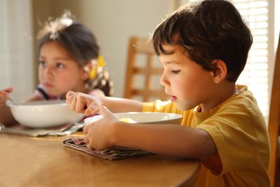 Two children eating at a table in soft sunlight.