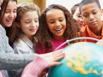 Children happily exploring a globe together in a classroom.