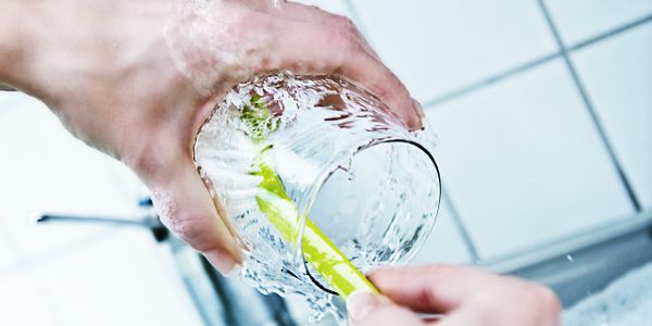 Hands cleaning a glass with a brush under running water.