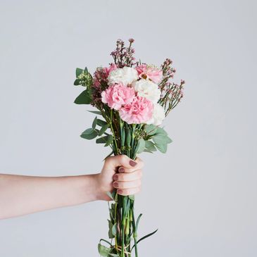 Hand holding a bouquet of pink and white flowers against a plain background.