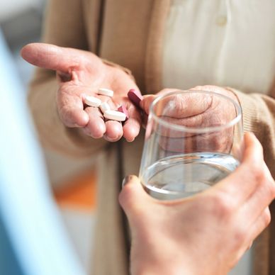 Two sets of hands. One is holding some tablets and the other is ready to pass over a glass of water