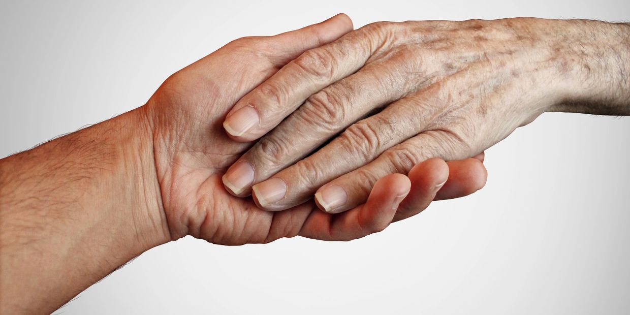 A young hand gently holding an elderly hand against a neutral background.