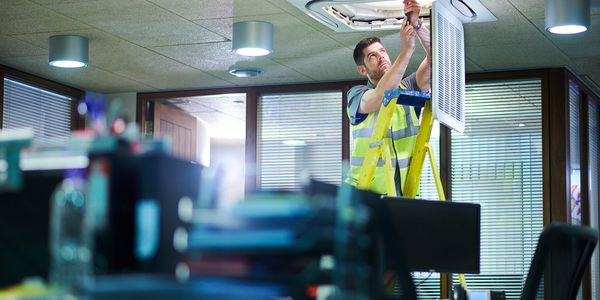 Technician changing office ceiling air filter.
