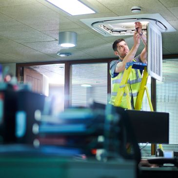 Technician fixing ceiling ventilation in an office.
