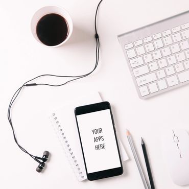 Workspace setup with phone, earphones, coffee, keyboard, and stationery.