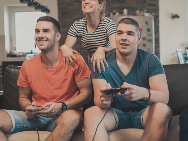 Three friends enjoying video games and smiling together on a couch.