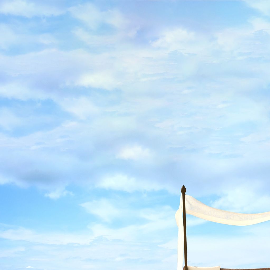 White fabric draped over a pole against a blue sky with clouds.