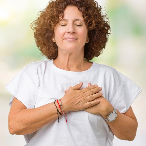 Woman in her 50's holding her hands on her heart with her eyes closed. 