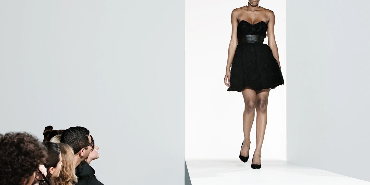 Model walking on runway in black dress.