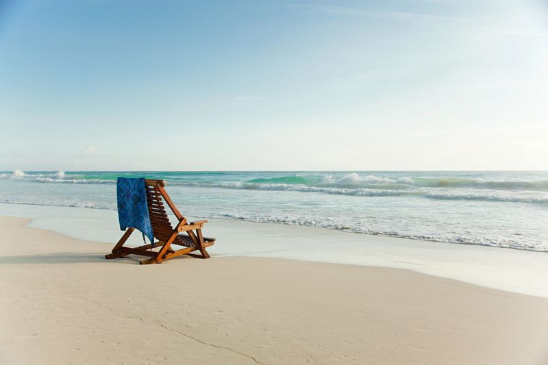 Deck chair on sandy beach at water's edge