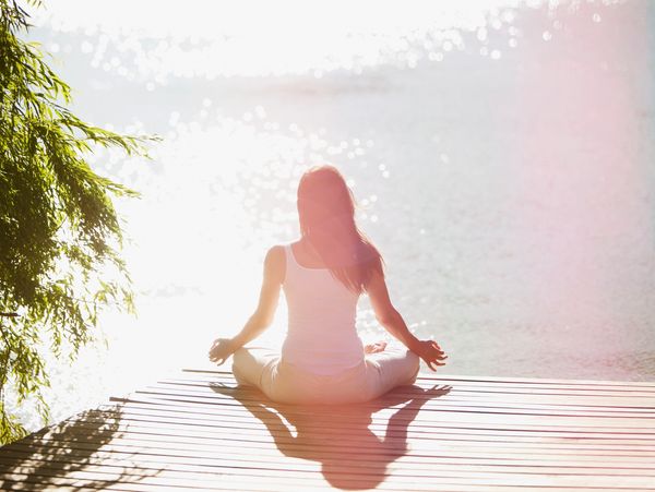Woman meditating by sparkling water on a wooden dock in sunlight.