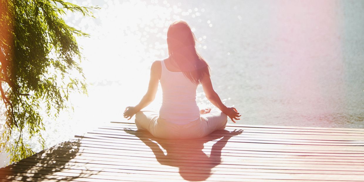 Woman meditating by sparkling water on a wooden dock in sunlight.