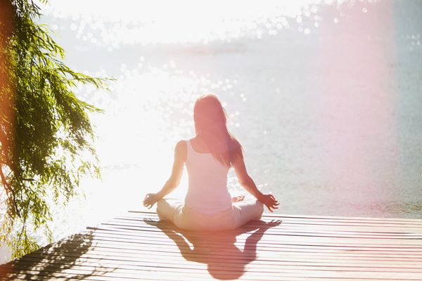 Woman meditating by the water on a sunny day.