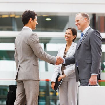 Business professionals shaking hands outdoors in a friendly meeting.