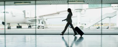 A woman walking through an airport terminal pulling a suitcase.