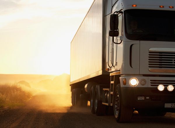 A large white truck driving on a dusty road at sunset.