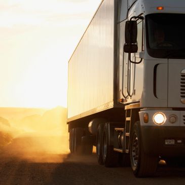 Semi truck driving on a dusty road at sunset.