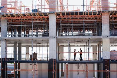 Two construction workers discuss plans inside a partially built structure.