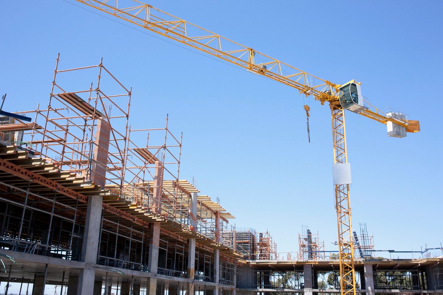A yellow construction crane working on a building site with scaffolding under a clear blue sky for oceancoast