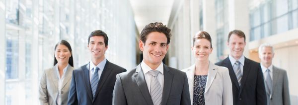 A group of six professionals smiling in a bright office hallway.