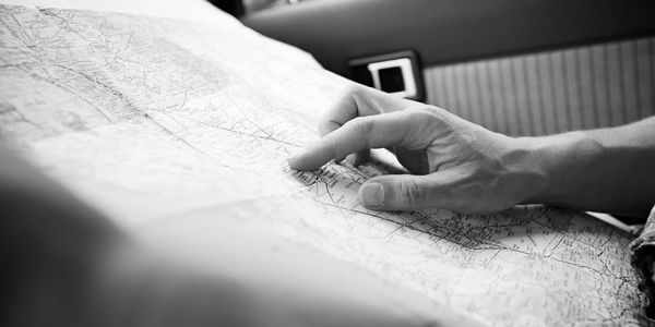 Person pointing at a location on a road map inside a car.