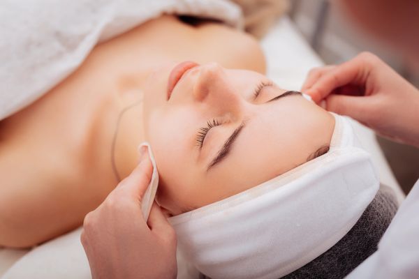 A woman receiving a gentle facial cleansing treatment at a spa.